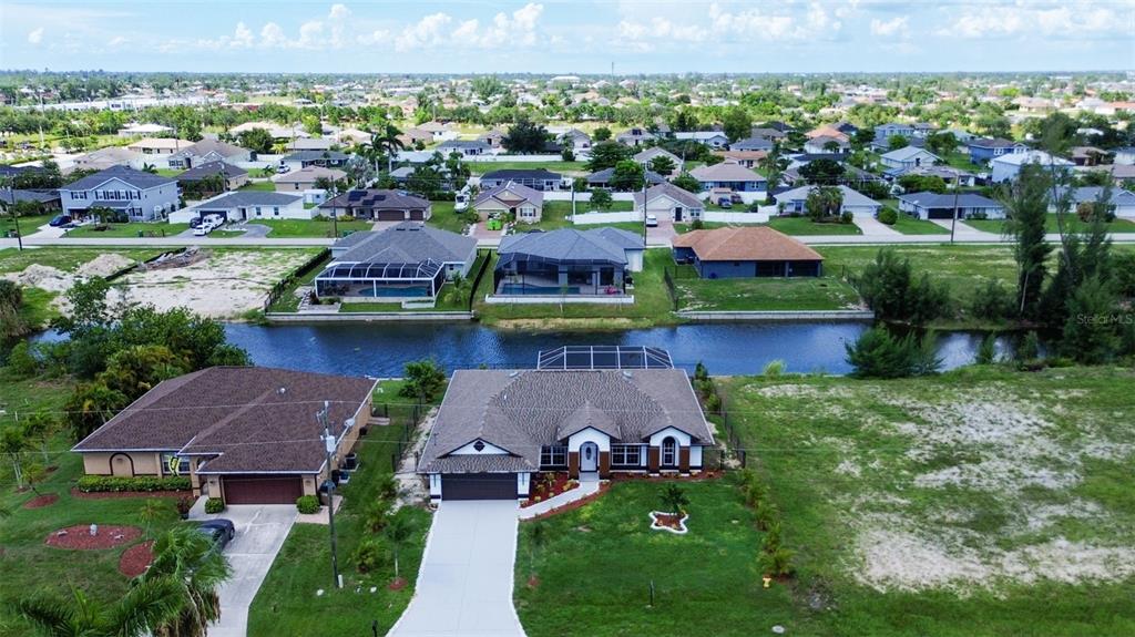 An aerial view shows a suburban neighborhood with houses, a canal, and vacant lots — 619 SW 26TH TERRACE, CAPE CORAL, FL