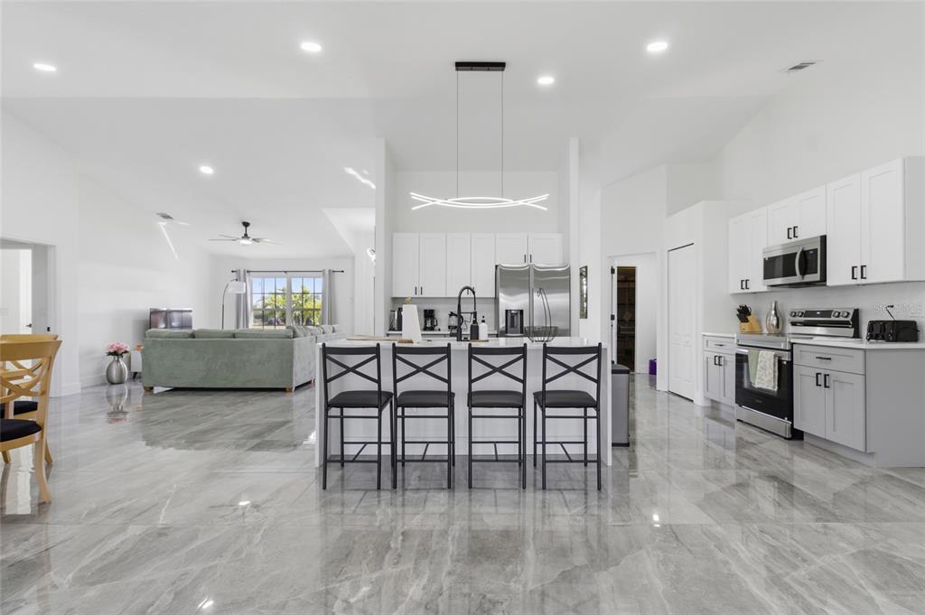 A modern open-concept kitchen features white cabinetry, a large island with four chairs, and gray tile flooring — 619 SW 26TH TERRACE, CAPE CORAL, FL