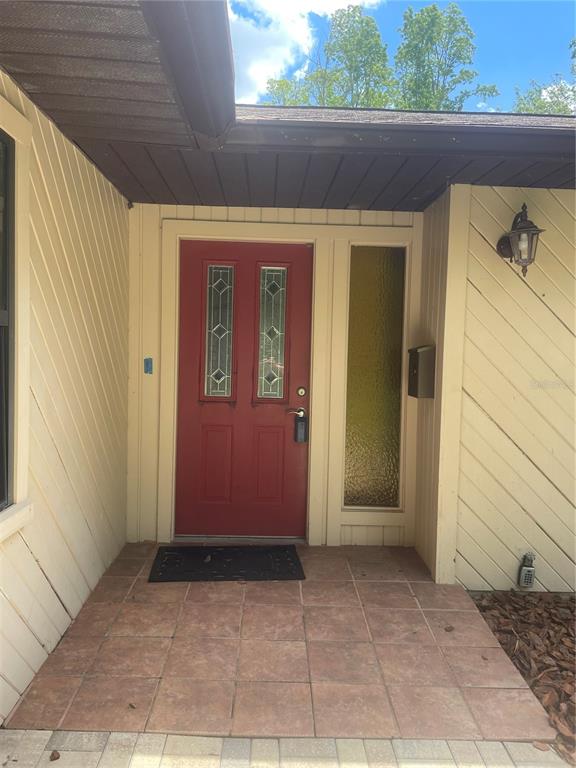 A single-story house with beige diagonal siding, brick accents, and a paved walkway — 2421 NW 106TH DRIVE, GAINESVILLE, FL
