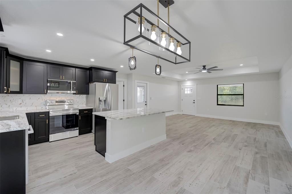 A modern kitchen features black cabinets, white marble-look countertops, and a large rectangular pendant light — 19226 BRANDON AVENUE, PORT CHARLOTTE, FL