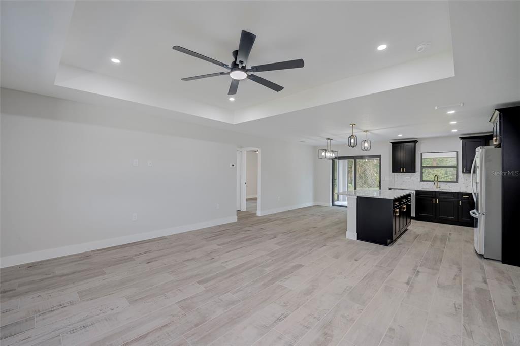A spacious open-concept living area features light wood-look tile flooring, a tray ceiling, and a kitchen — 19226 BRANDON AVENUE, PORT CHARLOTTE, FL