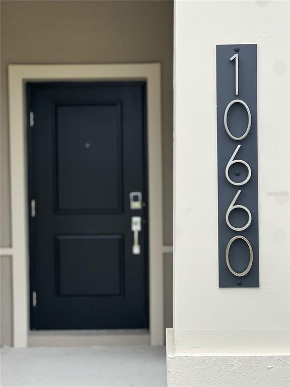 A dark front door is positioned next to a vertical plaque displaying the number 1060 — 10660 WORDS DRIVE, WINTER GARDEN, FL