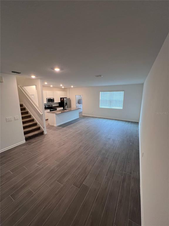 An open-concept living area features wood-look tile flooring, a kitchen with white cabinets, and stairs — 10660 WORDS DRIVE, WINTER GARDEN, FL