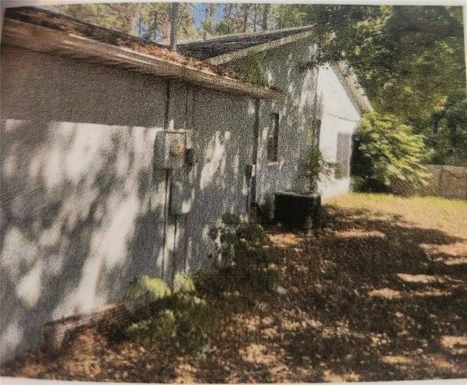 The exterior side of a house features a utility meter, an air conditioning unit, and trees — 11234 ELGIN BOULEVARD, SPRING HILL, FL