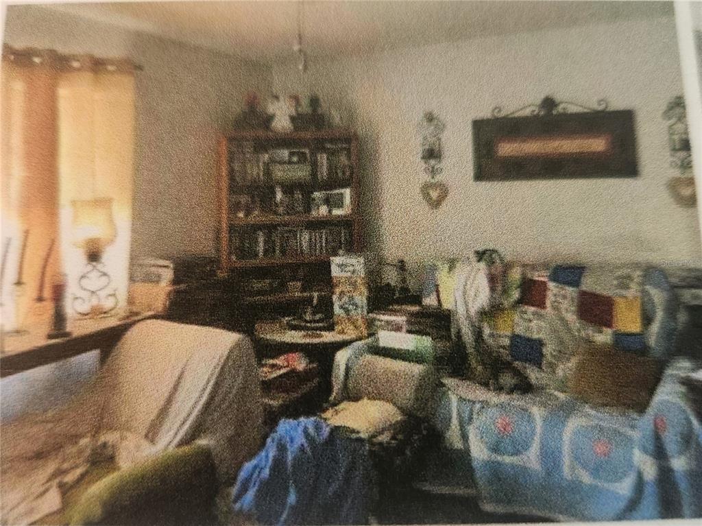 A cluttered living room features a wooden bookshelf, a patterned armchair, and wall decor — 11234 ELGIN BOULEVARD, SPRING HILL, FL