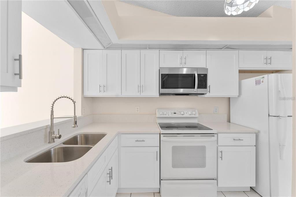 A kitchen with white cabinets, white appliances, a stainless steel microwave, and a double sink — 1113 LUCAYA CIRCLE, ORLANDO, FL