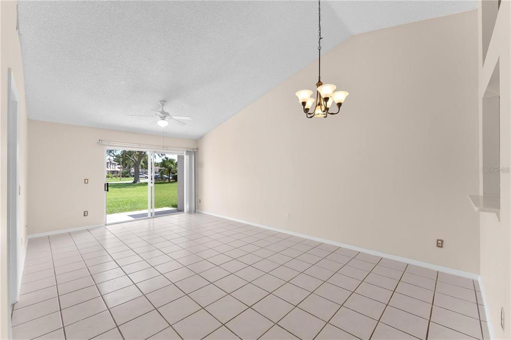 An empty room with light-colored tile flooring, a vaulted ceiling, a chandelier, and sliding doors — 1113 LUCAYA CIRCLE, ORLANDO, FL