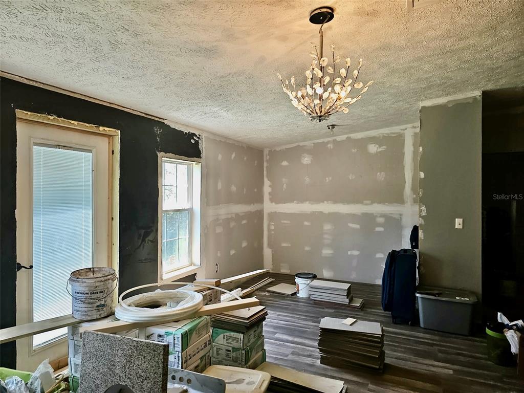 An unfinished room features drywall, a decorative chandelier, and new wood-look flooring — 6236 SPRINGWOODS LANE, LAKELAND, FL