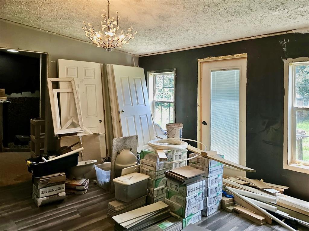 A room under renovation features dark walls, wood-look flooring, stacked building materials, and a chandelier — 6236 SPRINGWOODS LANE, LAKELAND, FL