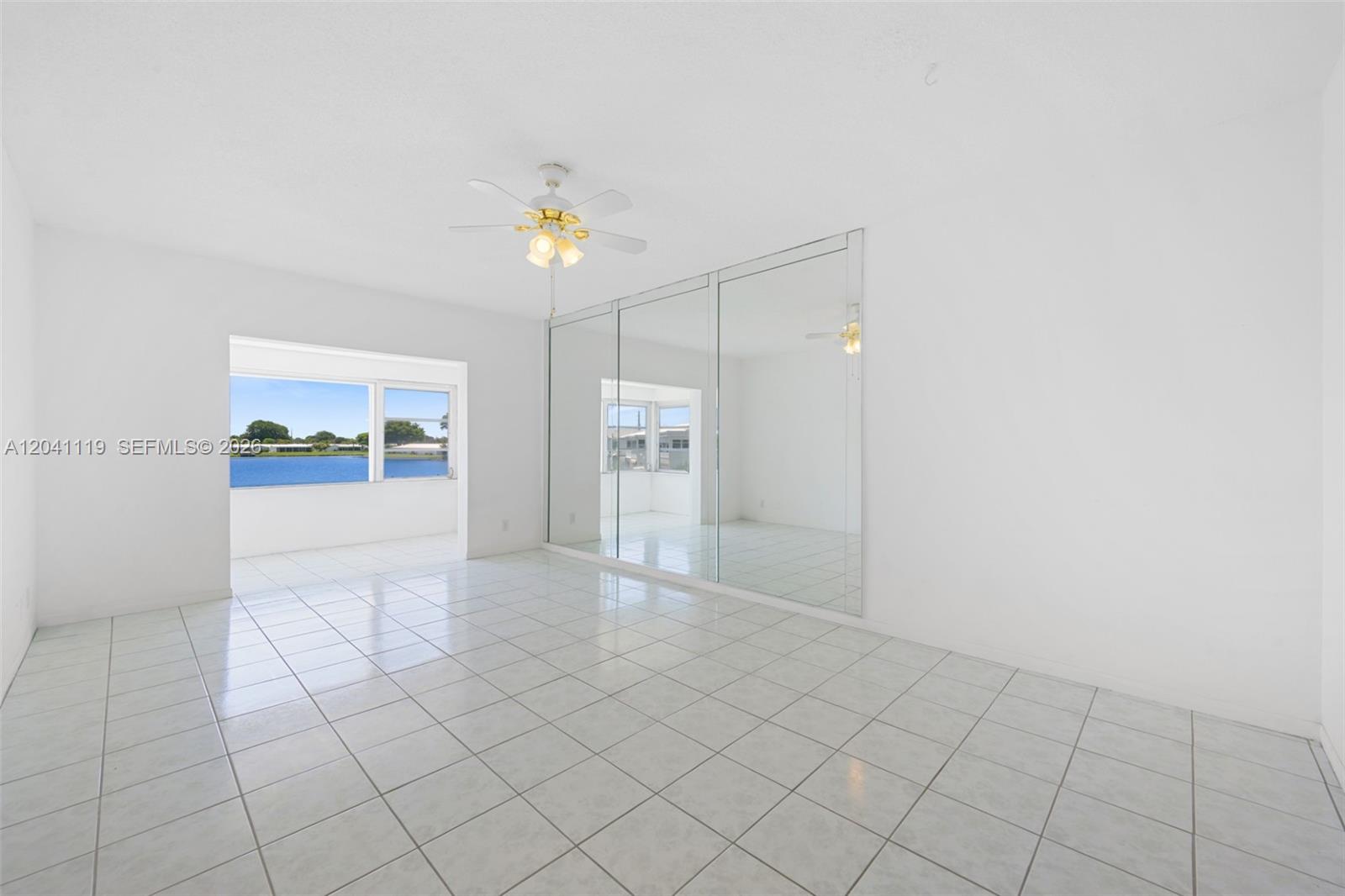 A bright, tiled room features a ceiling fan, mirrored closet doors, and a water view — 1116 Lake Ter # 208, Boynton Beach FL 33426, BOYNTON BEACH, FL
