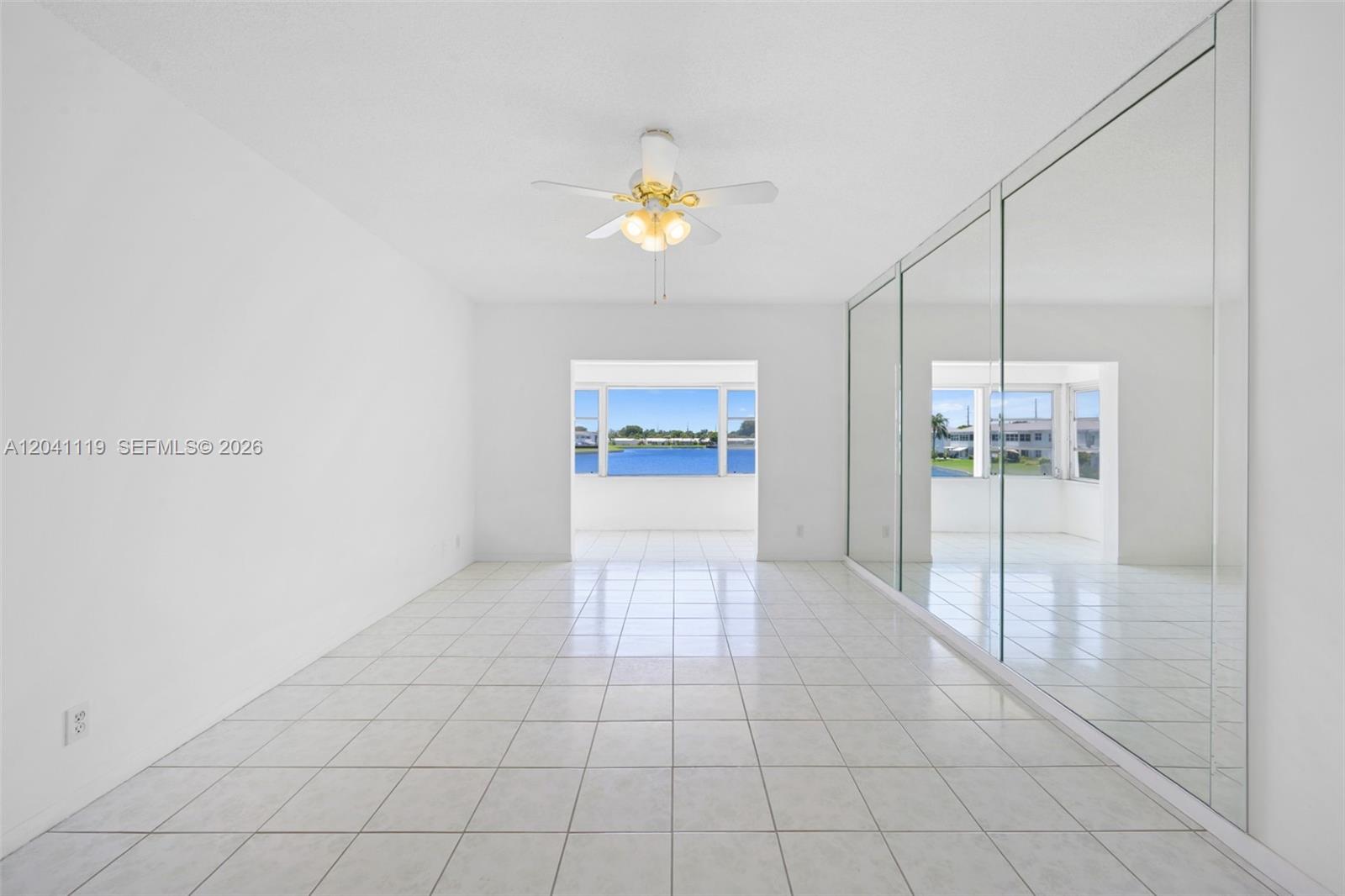 A bright room features white tile floors, a ceiling fan, and a mirrored closet wall — 1116 Lake Ter # 208, Boynton Beach FL 33426, BOYNTON BEACH, FL