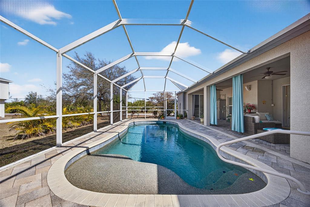 A screened-in swimming pool with a paved deck sits adjacent to a covered patio area — 9353 BLUEGILL CIRCLE, PORT CHARLOTTE, FL
