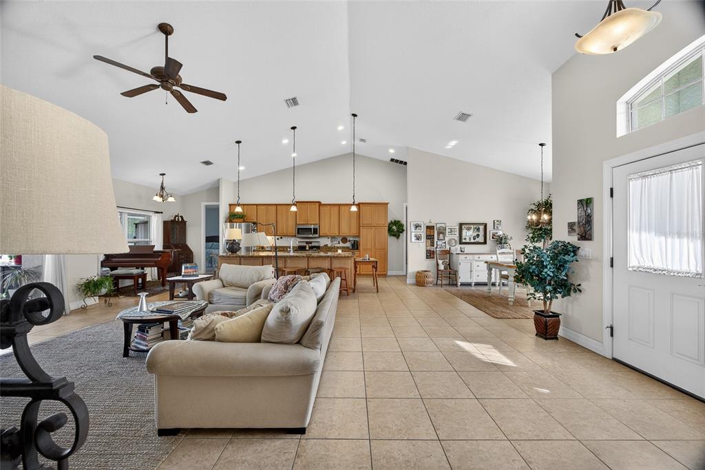 An open-concept living area features a vaulted ceiling, tile flooring, and a kitchen with cabinetry — 9353 BLUEGILL CIRCLE, PORT CHARLOTTE, FL