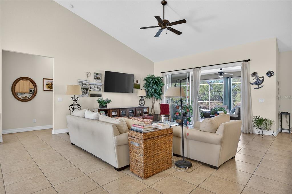 A living room features a vaulted ceiling, tile flooring, and sliding glass doors to a lanai — 9353 BLUEGILL CIRCLE, PORT CHARLOTTE, FL