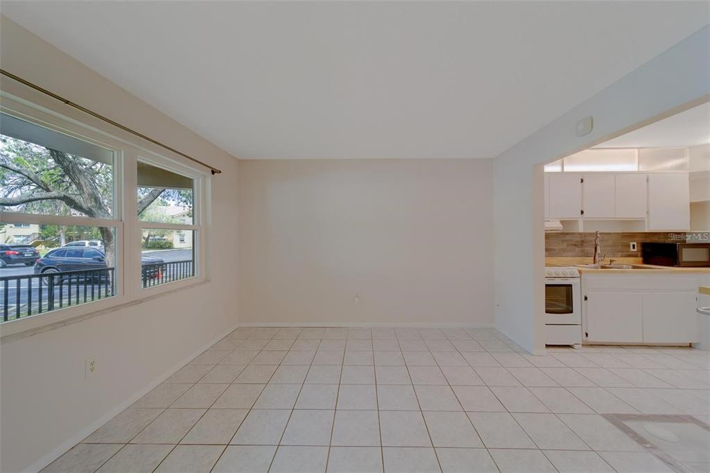 A dining area with white tile floors and large windows looks into a white kitchen — 2500 HARN BOULEVARD UNIT F12, CLEARWATER, FL