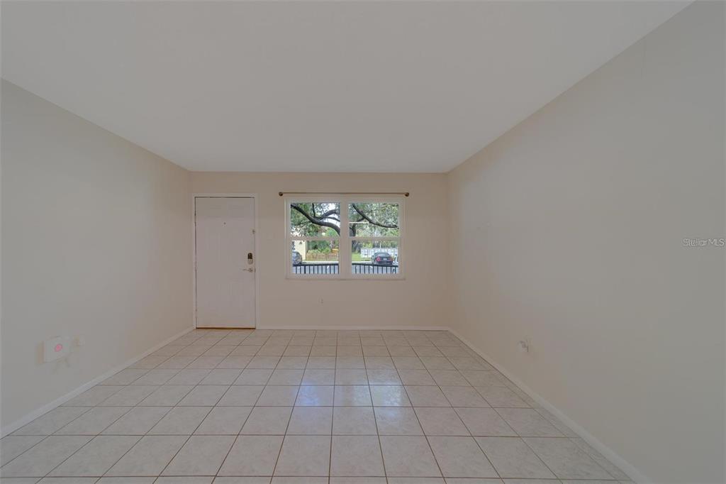 An empty room features light-colored tile flooring, beige walls, a white door, and a window — 2500 HARN BOULEVARD UNIT F12, CLEARWATER, FL