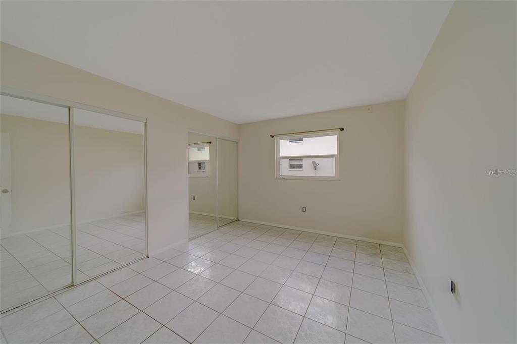A bedroom features white tile flooring, mirrored closet doors, and a single window — 2500 HARN BOULEVARD UNIT F12, CLEARWATER, FL