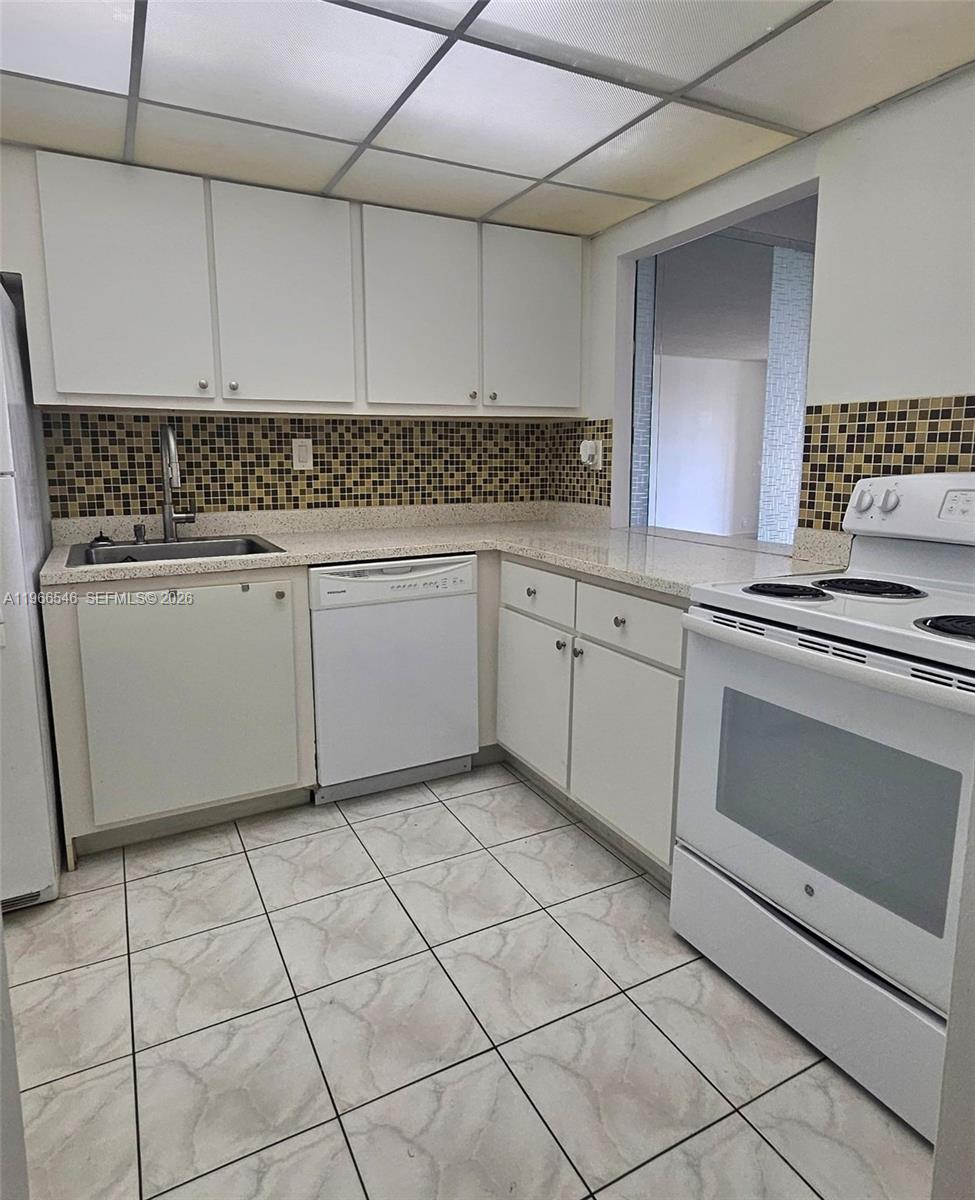 A kitchen features white cabinets, a mosaic tile backsplash, and white appliances — 1000 Parkview Dr # 605, Hallandale Beach FL 33009, HALLANDALE BEACH, FL