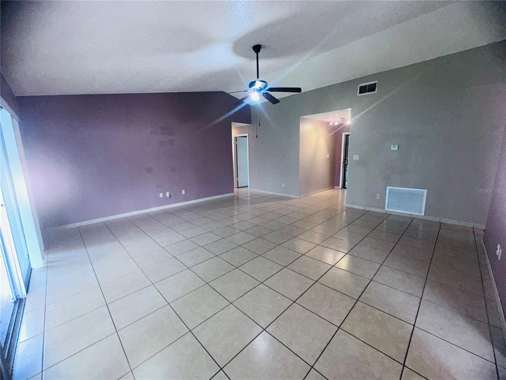 A spacious living room features vaulted ceilings, a ceiling fan, and light-colored tile flooring — 12123 AGANA STREET, ORLANDO, FL