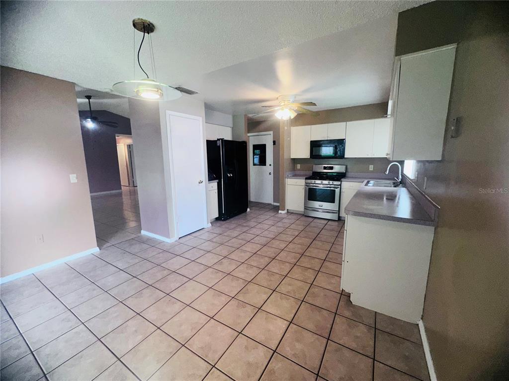 A kitchen with tile flooring, white cabinets, stainless steel appliances, and a black refrigerator — 12123 AGANA STREET, ORLANDO, FL