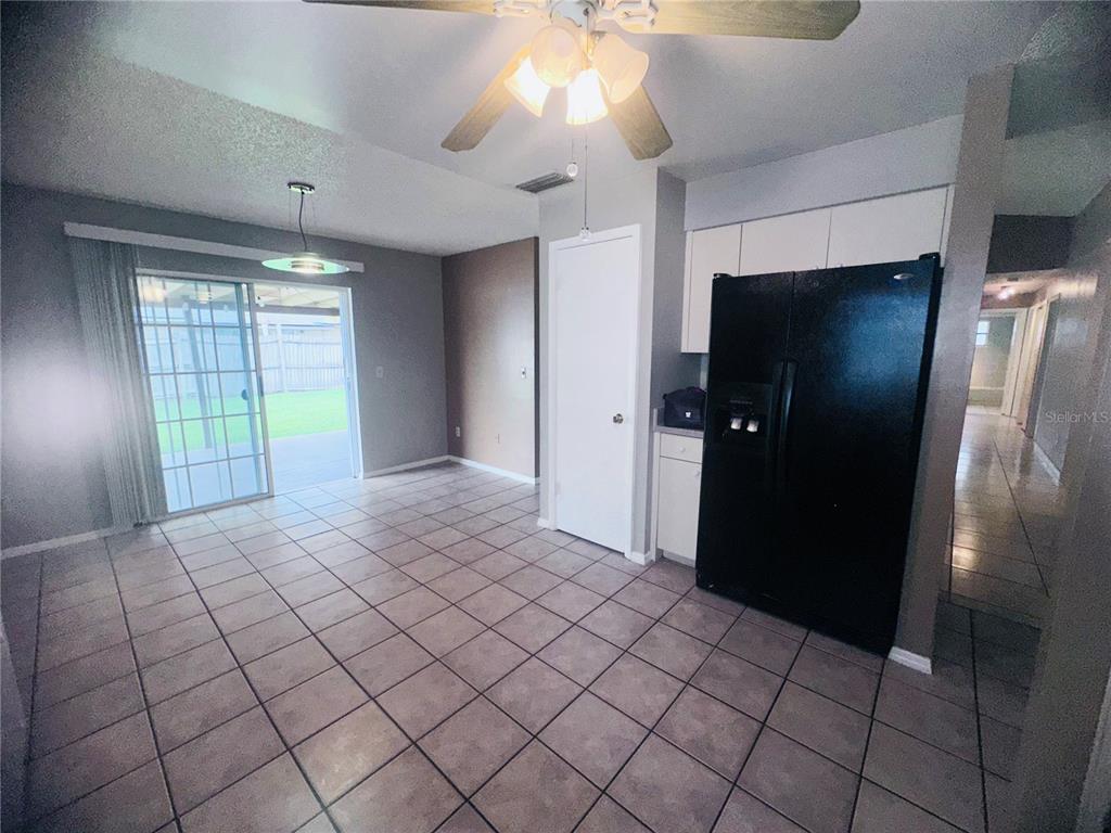 A tiled kitchen and dining area features a black refrigerator, white cabinets, and sliding glass doors — 12123 AGANA STREET, ORLANDO, FL