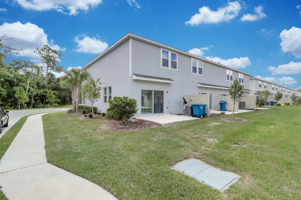 The exterior of a two-story gray townhouse features a concrete patio and a grassy yard — 3010 CANARY AVENUE, DAVENPORT, FL