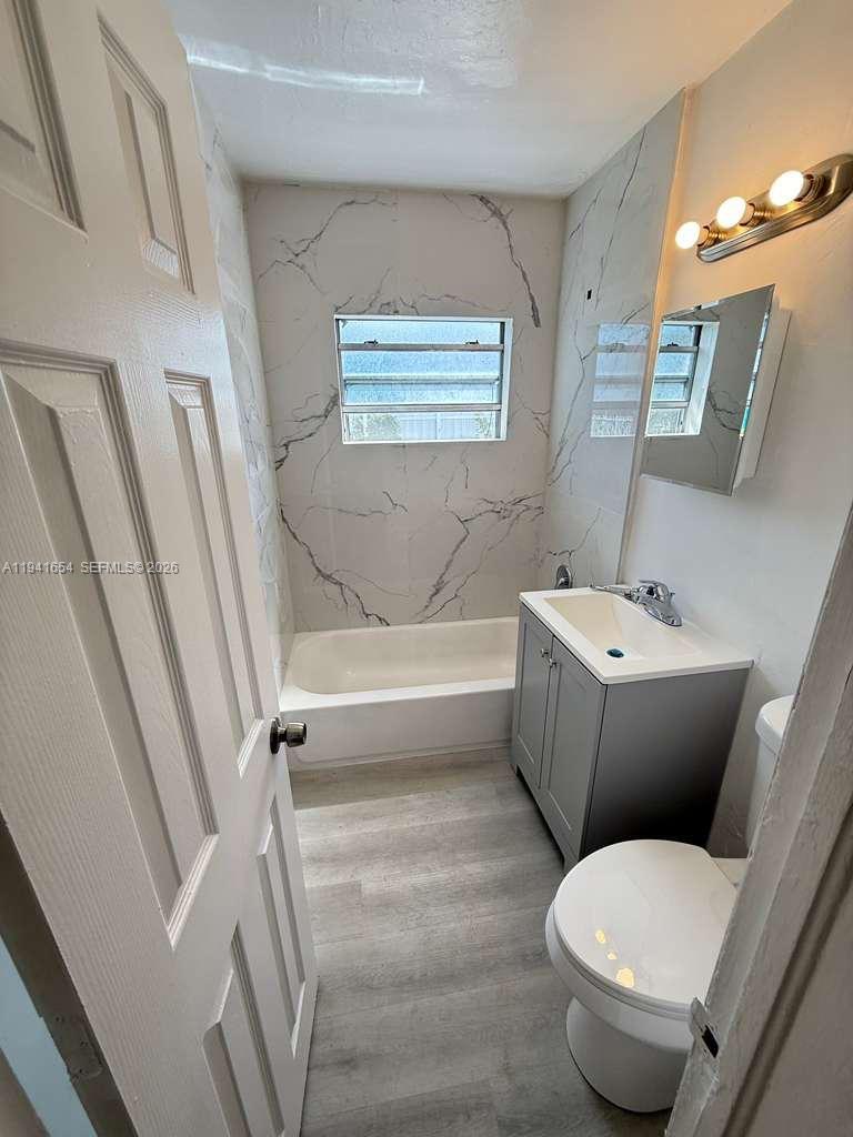 A small bathroom features a gray vanity, a white toilet, and a marble-tiled bathtub area — 6720 NW 6th Ct # 6720, Miami FL 33150, MIAMI, FL