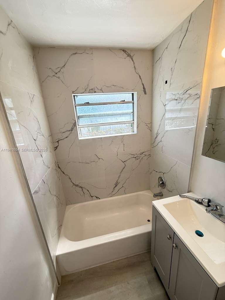 A bathroom features a white bathtub with marble-patterned tile walls and a gray vanity — 6720 NW 6th Ct # 6720, Miami FL 33150, MIAMI, FL