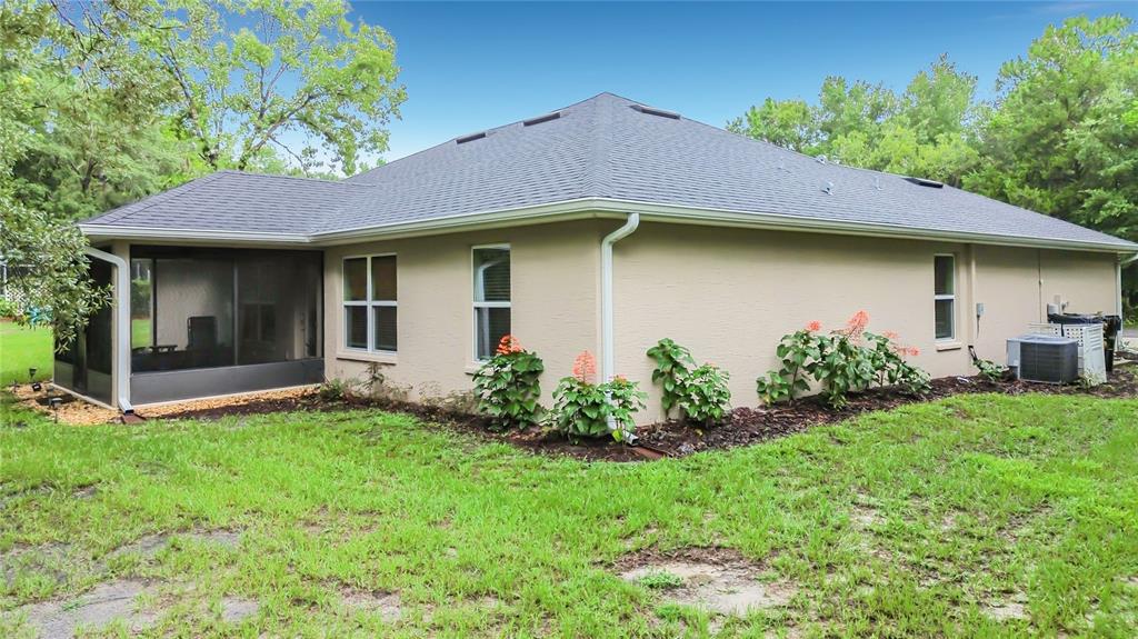 The exterior of a beige house features a screened-in porch, a shingled roof, and landscaping — 28 HOLLY COURT, HOMOSASSA, FL