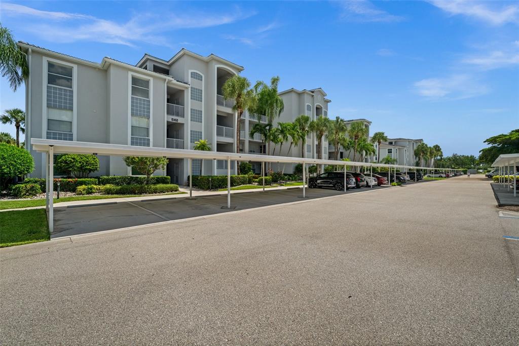 A multi-story apartment building features covered parking spaces in the foreground under a sunny sky — 10460 WASHINGTONIA PALM WAY UNIT 1342, FORT MYERS, FL