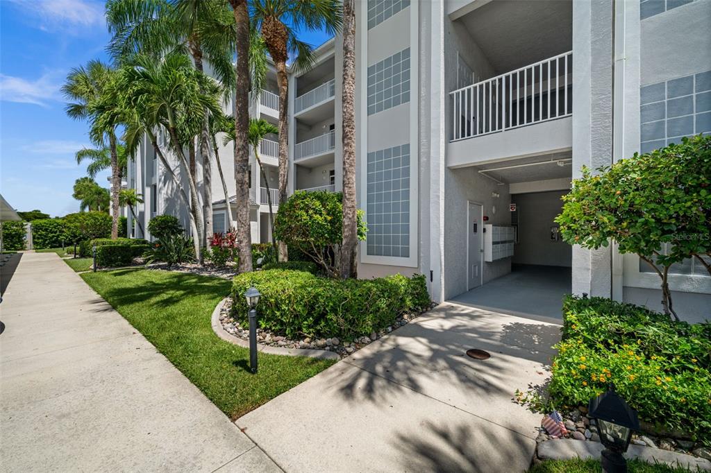 A multi-story apartment building exterior features a concrete walkway, palm trees, and a mail area — 10460 WASHINGTONIA PALM WAY UNIT 1342, FORT MYERS, FL