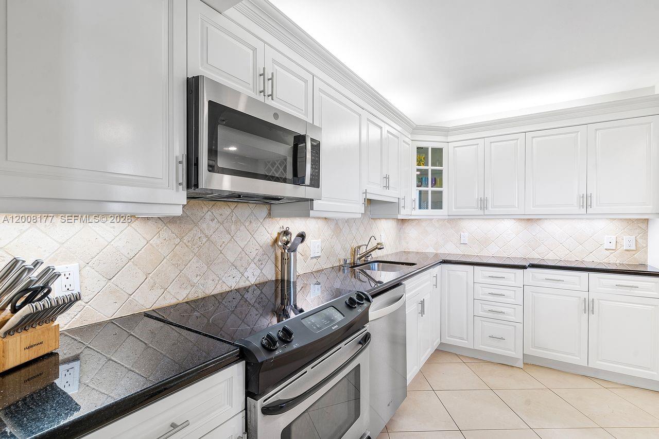 A white kitchen features black countertops, stainless steel appliances, and a tiled backsplash — 400 Ocean Trail Way # 302, Jupiter FL 33477, JUPITER, FL
