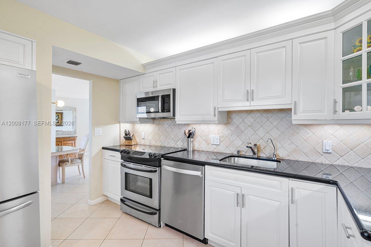 A kitchen features white cabinetry, black countertops, stainless steel appliances, and a tiled backsplash — 400 Ocean Trail Way # 302, Jupiter FL 33477, JUPITER, FL