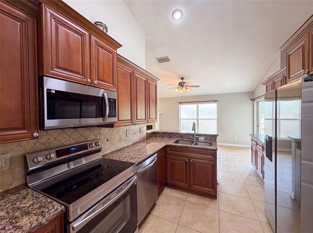 A kitchen features wood cabinets, granite countertops, stainless steel appliances, and tile flooring — 17802 JEFFERSON STREET, WINTER GARDEN, FL
