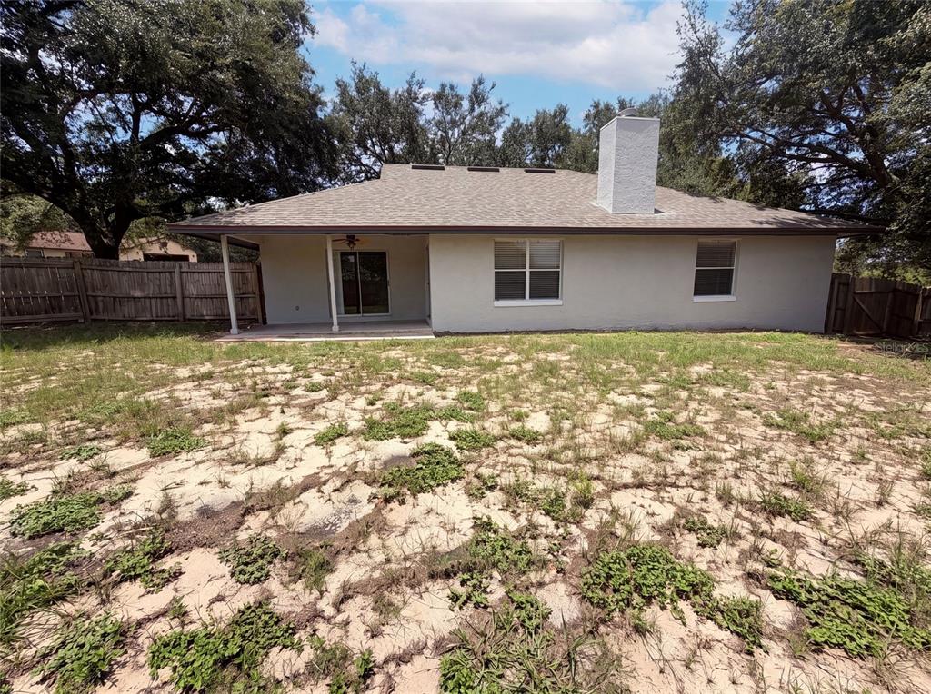 The rear exterior of a single-story house features a covered patio, chimney, and sandy yard — 17802 JEFFERSON STREET, WINTER GARDEN, FL
