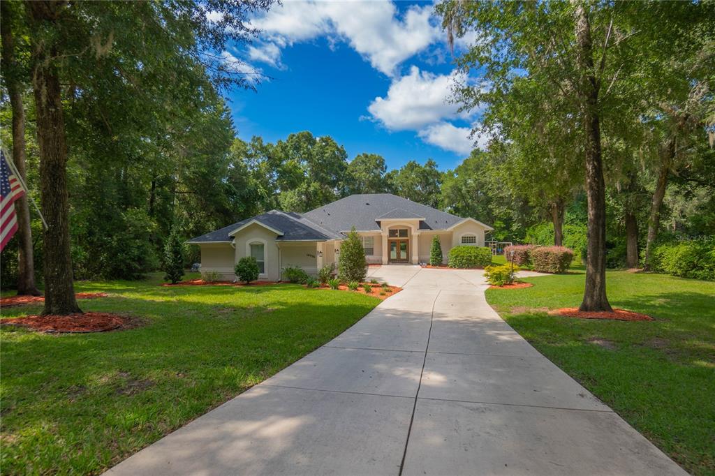 A single-story house with a concrete driveway sits on a grassy lot with many trees — 18976 SW 93RD LOOP, DUNNELLON, FL