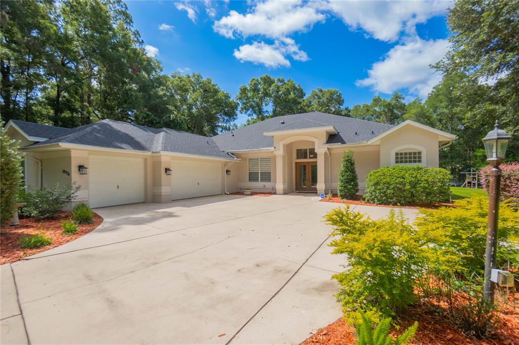 A single-story house with a three-car garage and a concrete driveway under a blue sky — 18976 SW 93RD LOOP, DUNNELLON, FL