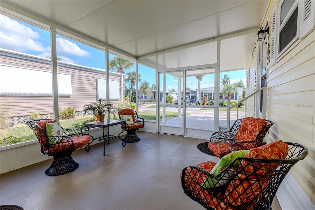 A screened-in porch features four wicker chairs with orange cushions and a small metal table — 2100 KINGS HIGHWAY UNIT 283, PORT CHARLOTTE, FL