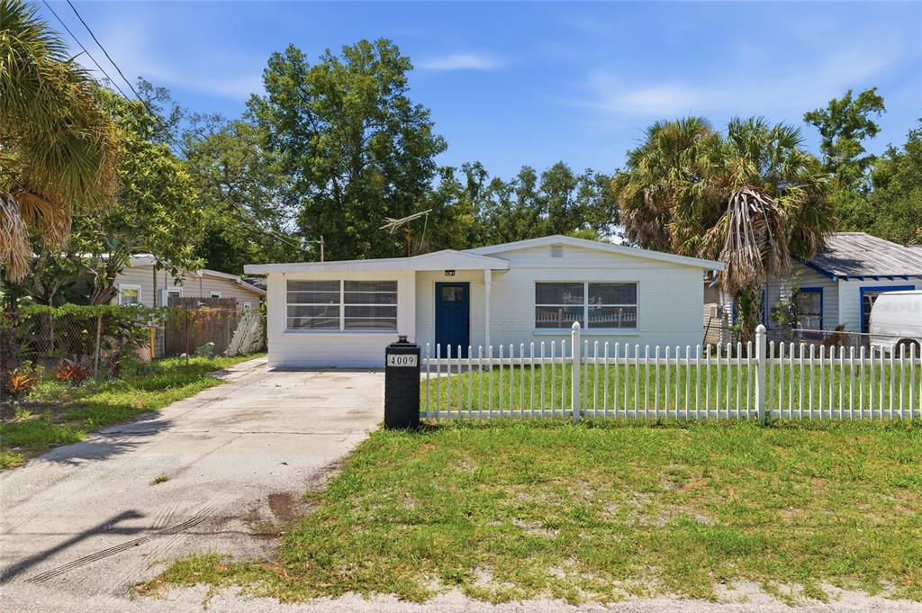 A single-story white house with a blue front door and a white picket fence — 4009 E POWHATAN AVENUE, TAMPA, FL
