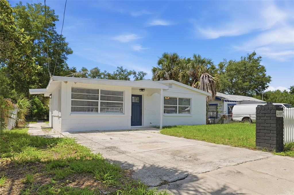 A white, single-story house with a concrete driveway and a dark blue front door — 4009 E POWHATAN AVENUE, TAMPA, FL