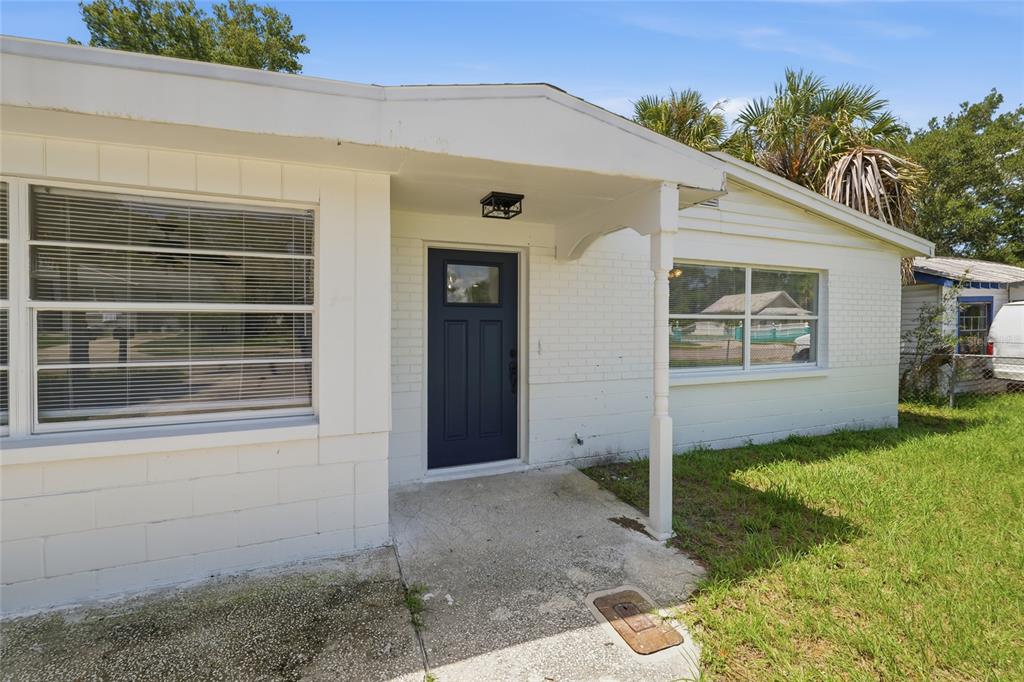 A white brick house exterior features a dark blue front door and a covered porch — 4009 E POWHATAN AVENUE, TAMPA, FL