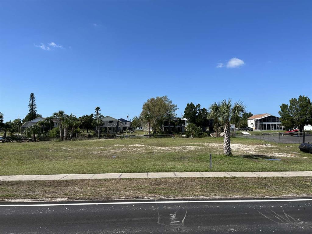 A vacant, grassy residential lot sits along a paved road under a clear blue sky — 3341 SHOAL LINE BOULEVARD, HERNANDO BEACH, FL