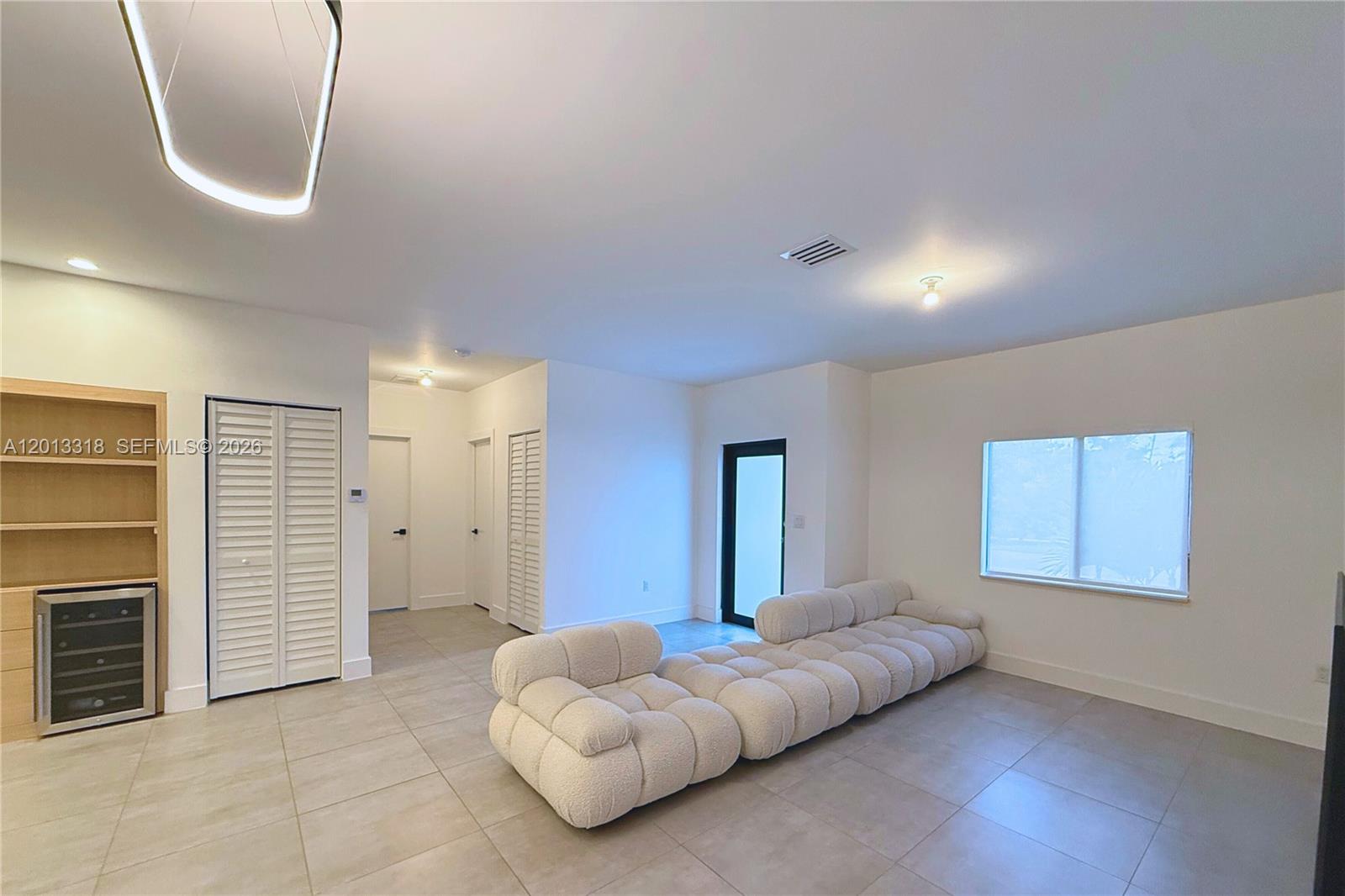 This living room features light tile flooring, a white modular sofa, and a wine cooler — 233 NW 120th St, Miami FL 33168, MIAMI, FL