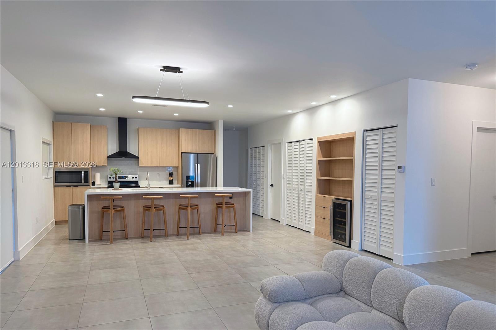 A modern kitchen features light wood cabinetry, a central island with bar stools, and tile flooring — 233 NW 120th St, Miami FL 33168, MIAMI, FL