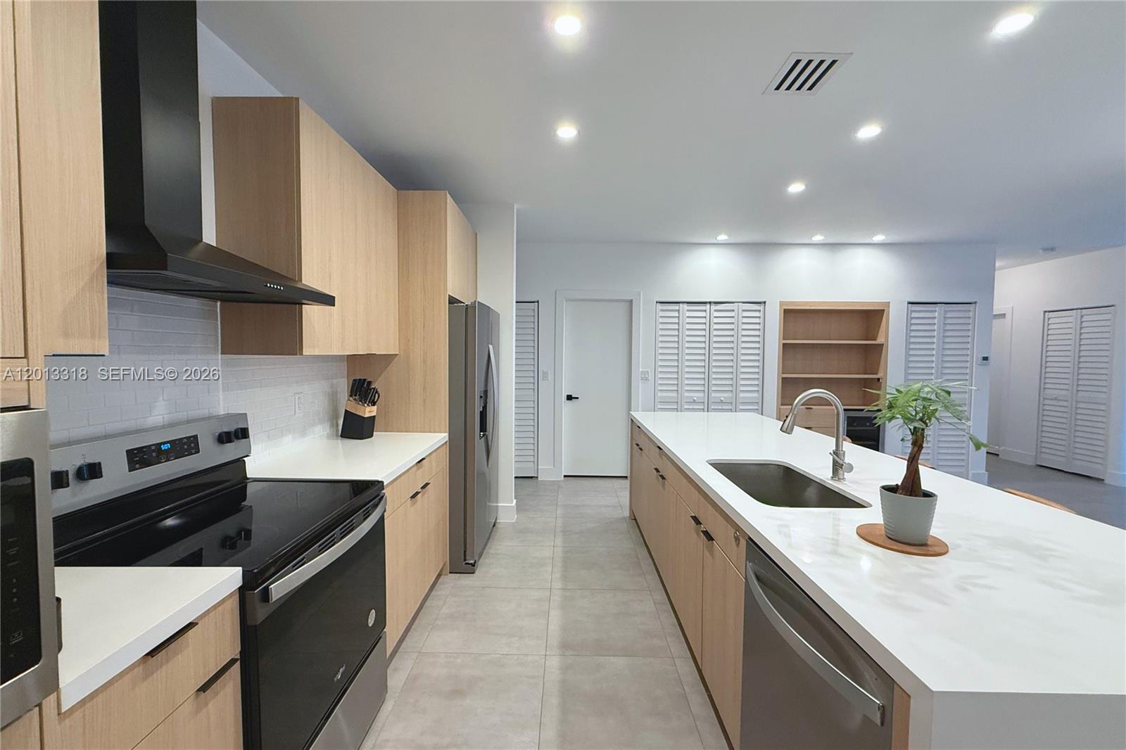 A modern kitchen features light wood cabinets, stainless steel appliances, and a large white island — 233 NW 120th St, Miami FL 33168, MIAMI, FL