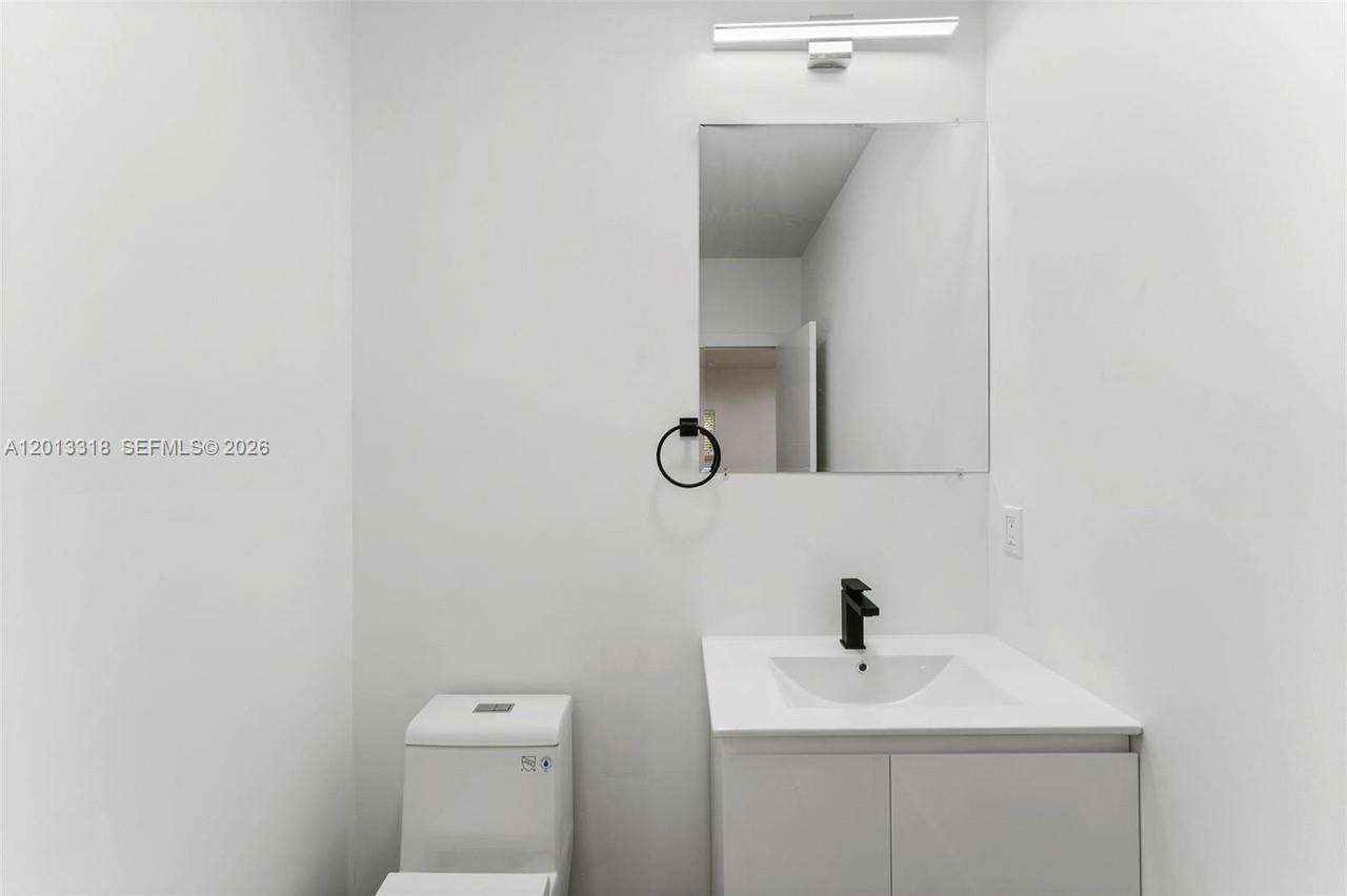 A modern bathroom features a white vanity, black faucet, square mirror, and a white toilet — 233 NW 120th St, Miami FL 33168, MIAMI, FL