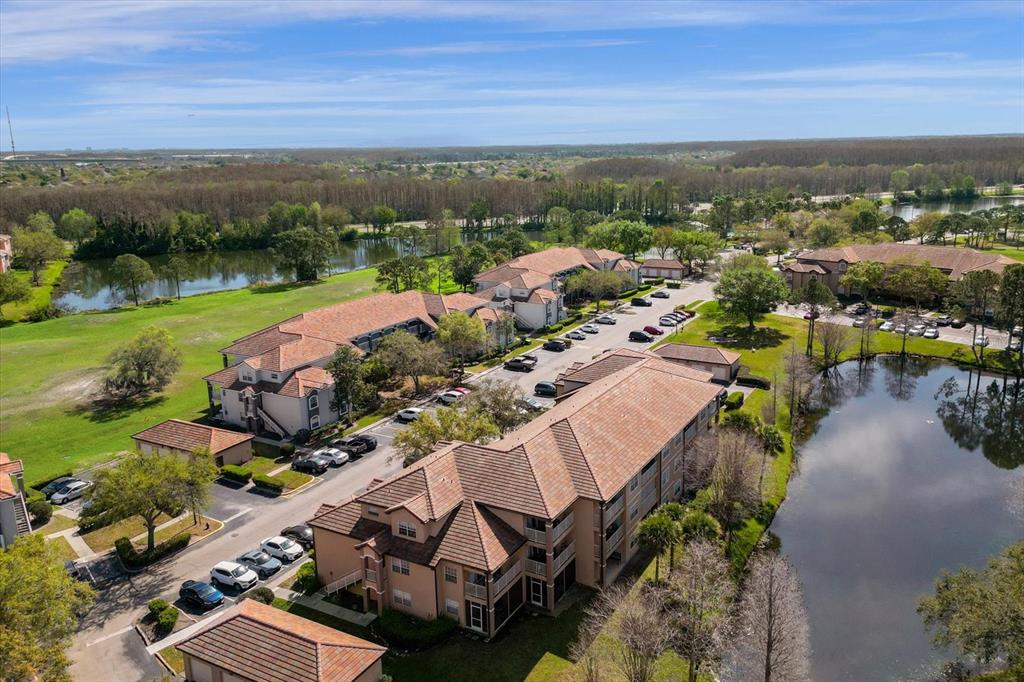 An aerial view shows multi-story apartment buildings with tile roofs surrounded by ponds and trees — 14036 FAIRWAY ISLAND DR UNIT 1513, ORLANDO, FL