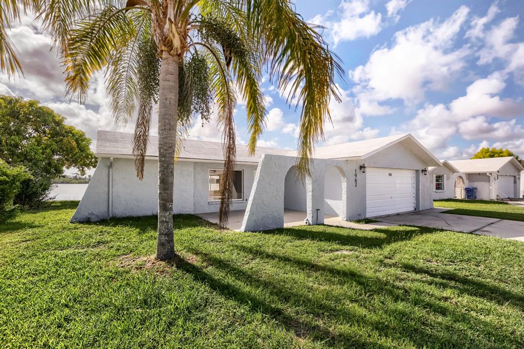 A light blue single-story house with a palm tree and an arched entryway — 1962 SOCIETY DRIVE, HOLIDAY, FL