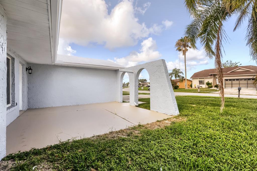 A concrete patio features two arched architectural structures against a light blue exterior wall — 1962 SOCIETY DRIVE, HOLIDAY, FL