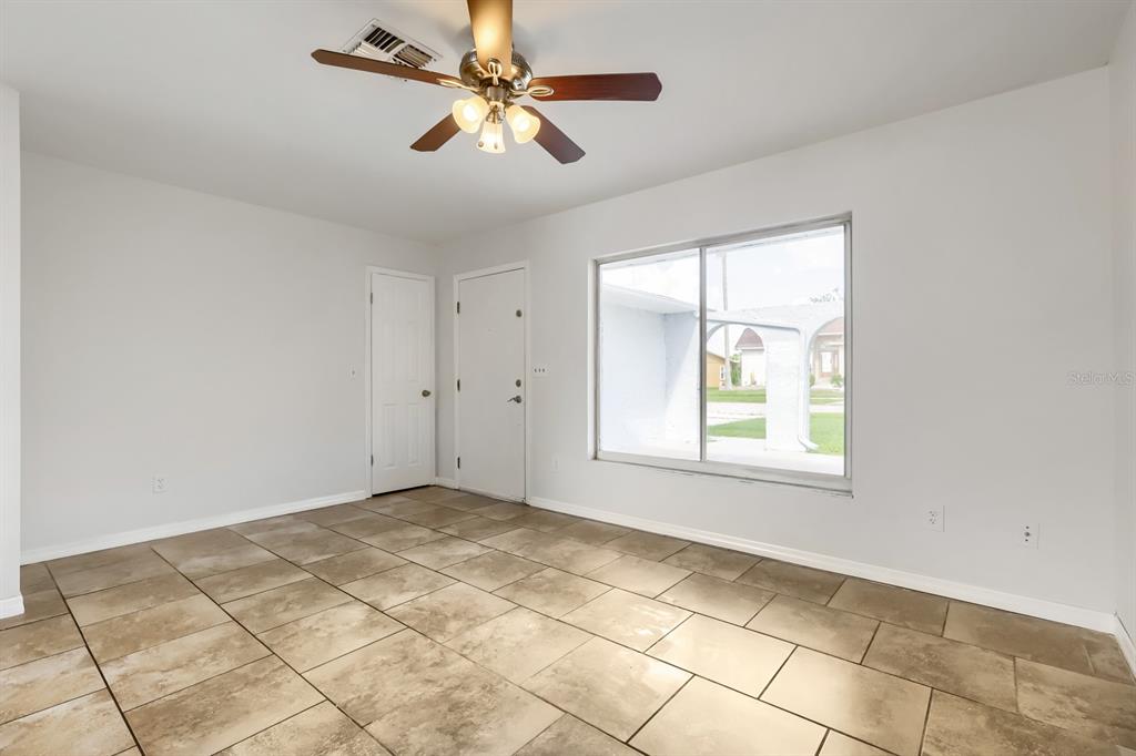 An empty room features light-colored walls, large floor tiles, a ceiling fan, and a window — 1962 SOCIETY DRIVE, HOLIDAY, FL